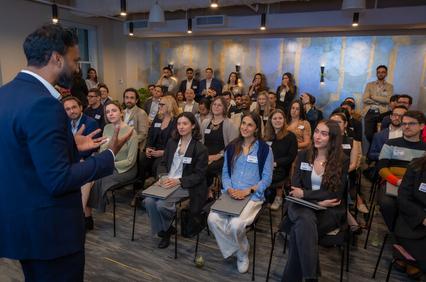 A speaker addresses a large audience in a modern conference room.