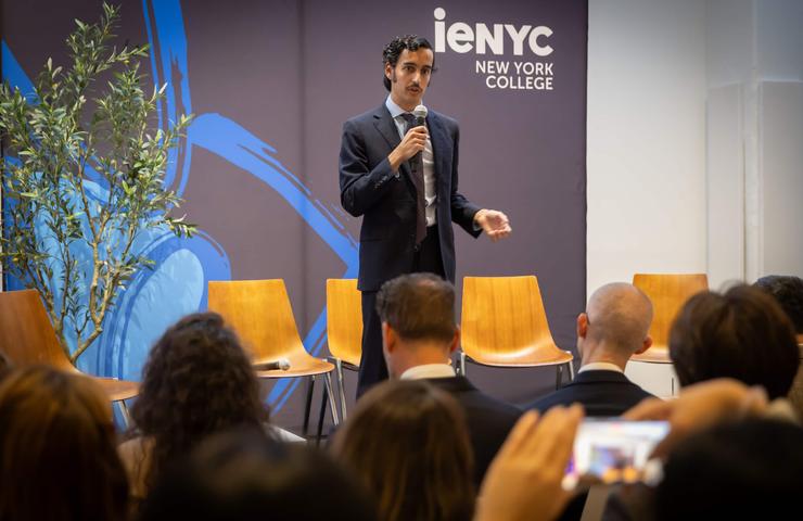 A speaker addresses an audience at an event in a college setting.