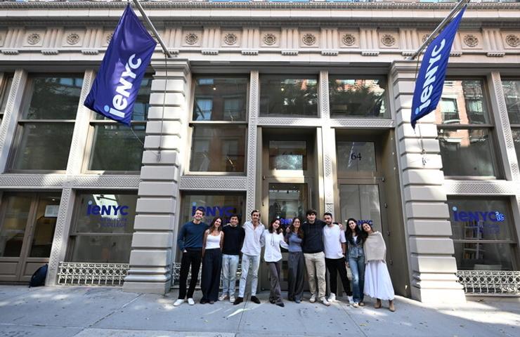 A diverse group of people stands together outside a building with prominent banners.