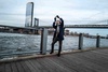 A person is taking a picture with a smartphone by a river with a bridge in the background.