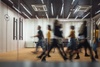 Blurry motion of busy people walking in a modern office corridor with wooden decor and glass partitions.