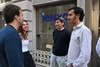 A group of young people are chatting and smiling outside a building with a sign.
