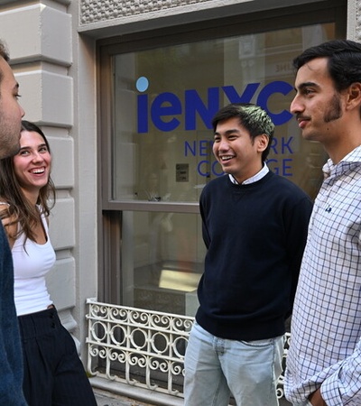 A group of young people are chatting and smiling outside a building with a sign.