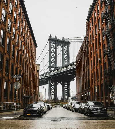 A view of the Manhattan Bridge framed by brick buildings on a cloudy day.