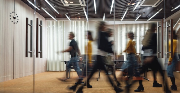 Blurry motion of busy people walking in a modern office corridor with wooden decor and glass partitions.