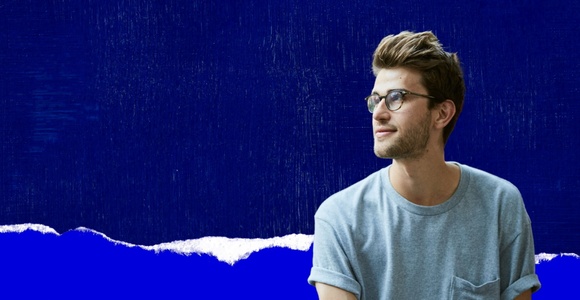 A young man with glasses is looking to the side against a blue background.